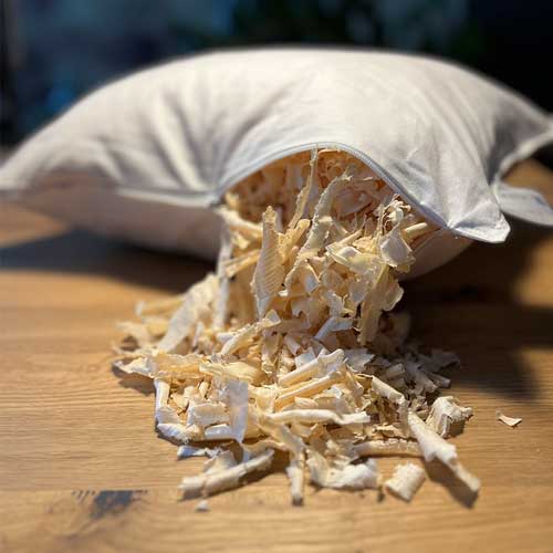 Ein geöffnetes Kissen liegt auf einem Tisch und ist mit Arvenholzspänen gefüllt, die herausfallen.
