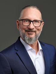 Schlafexperte Gregor Ott - mit Brille und grauem Bart trägt einen blauen Anzug und lächelt.